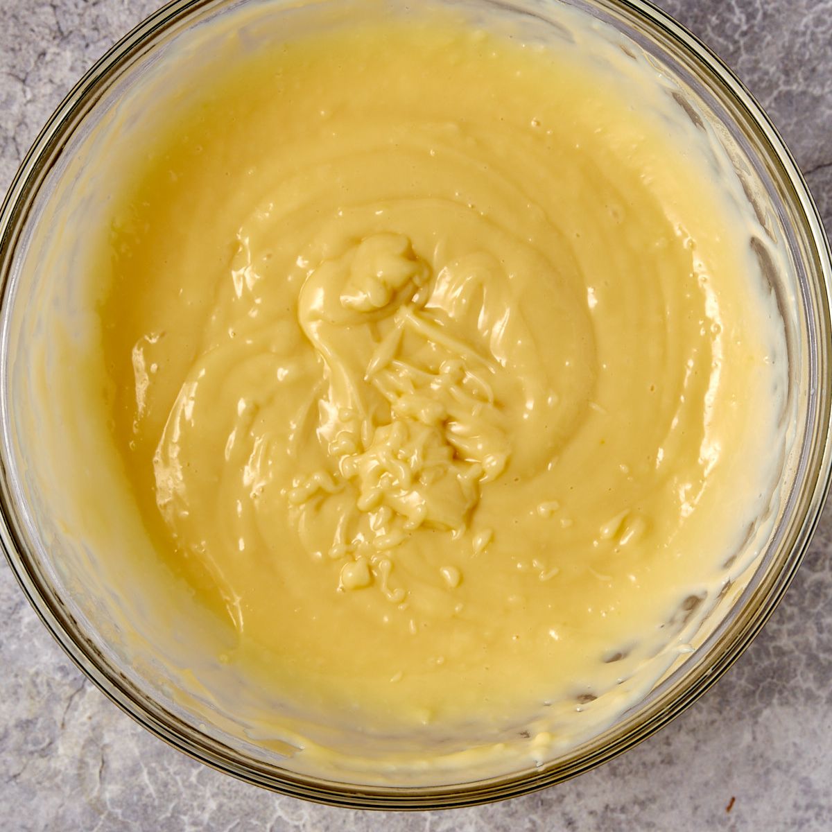 Thick from-scratch vanilla pudding cooling in a glass bowl.