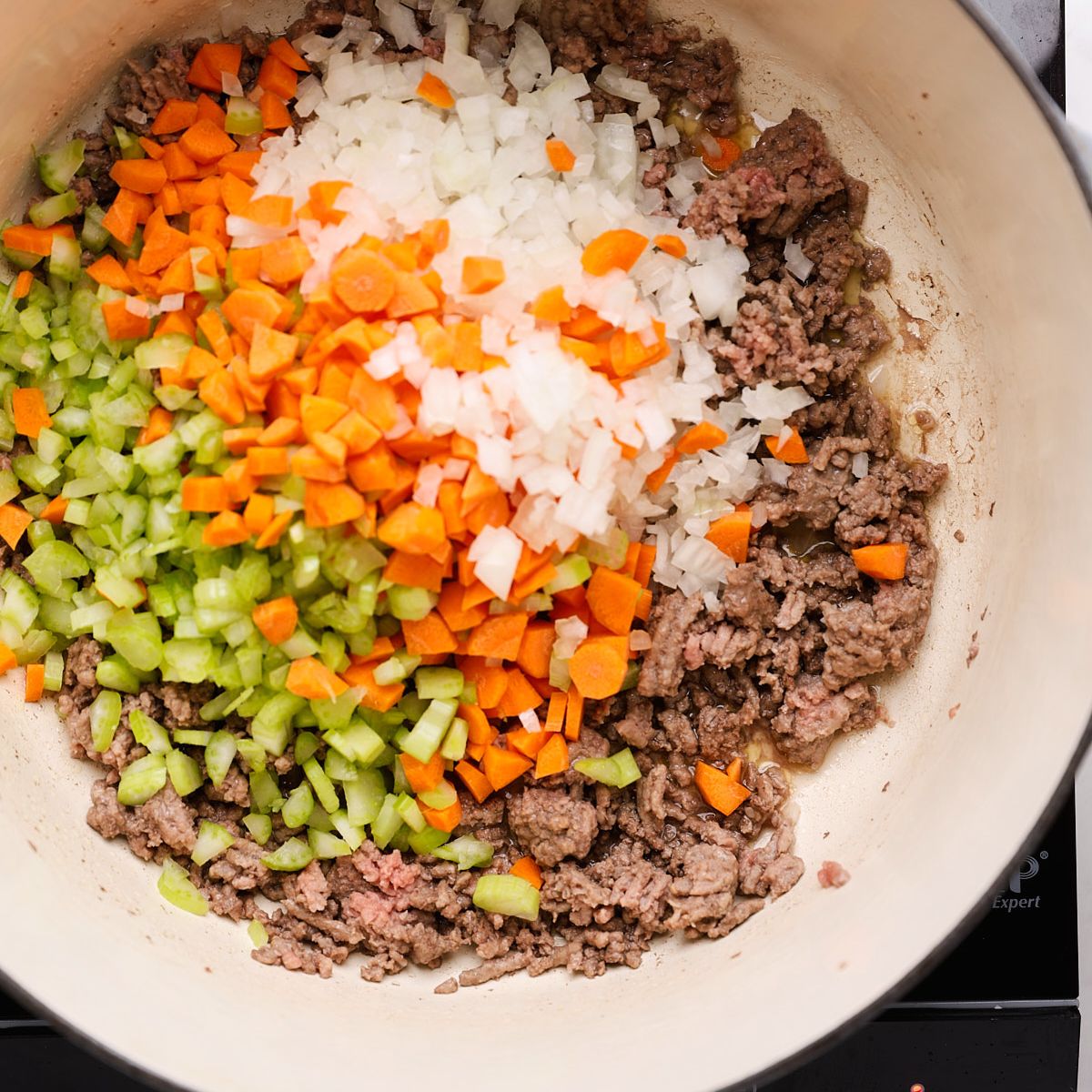 Diced onion, carrots, and celery cooking with browned ground beef in a Dutch oven.
