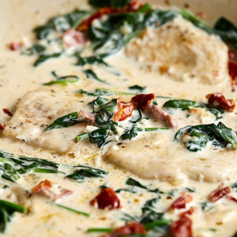 Creamy chicken breast in a rich sauce with wilted spinach and sun-dried tomatoes, garnished with cracked black pepper.