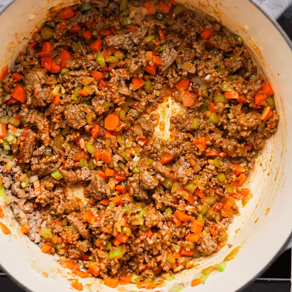 Ground beef and diced vegetables cooking in a Dutch oven.