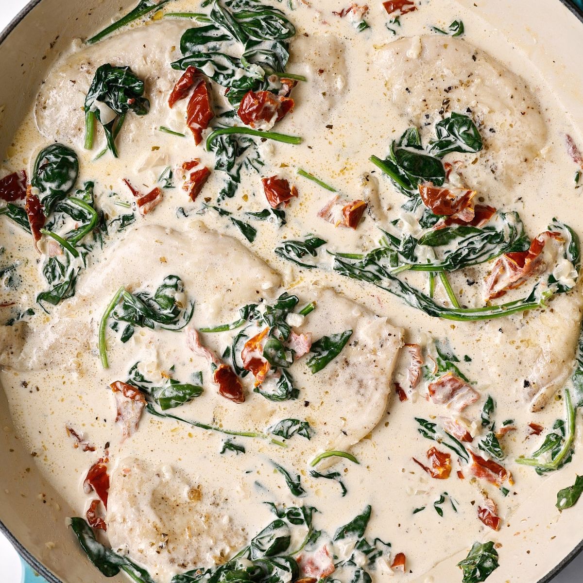 Seared chicken cutlets returned to the skillet, spooned over with creamy spinach and sun-dried tomato sauce.