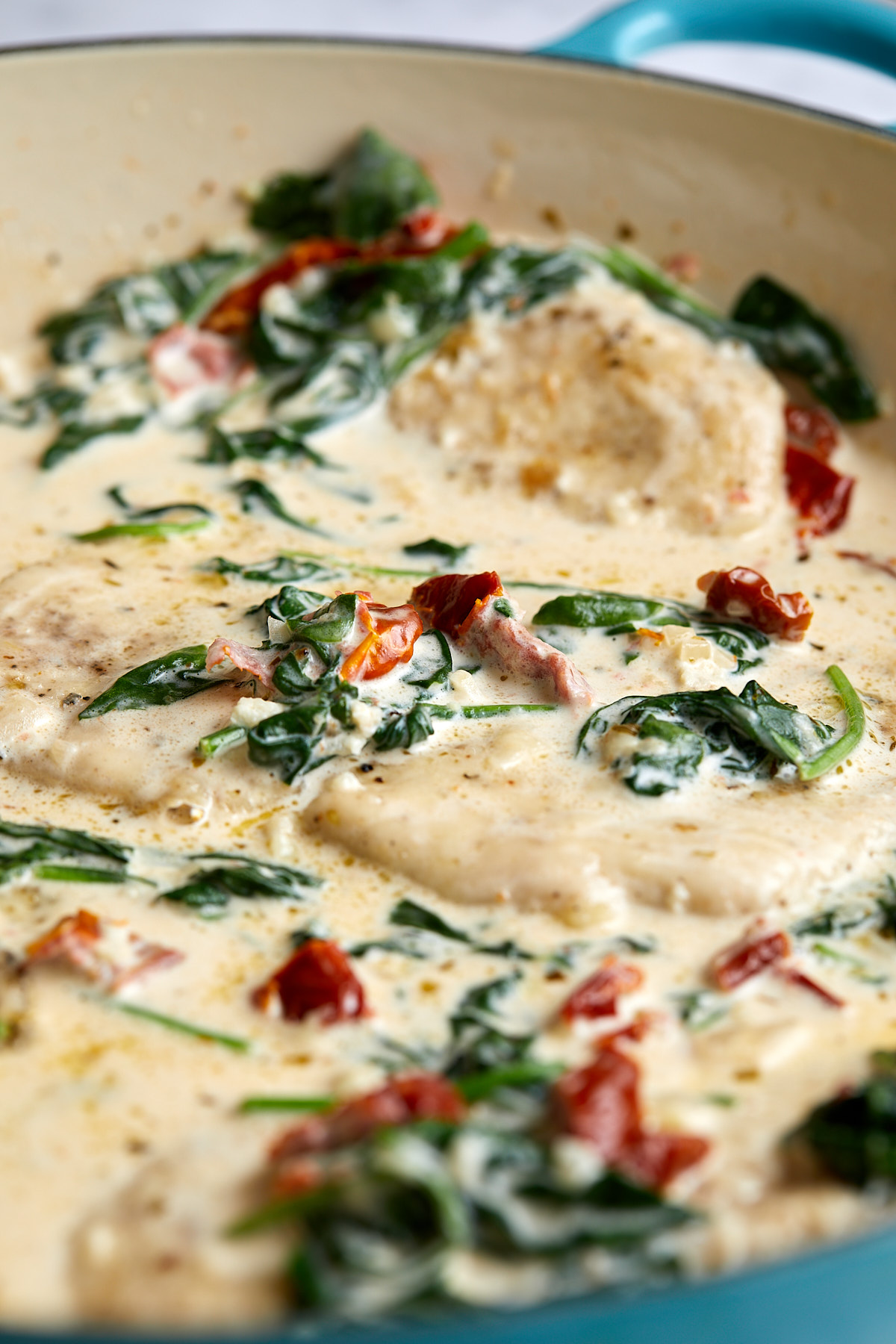 Creamy Tuscan chicken on a white plate, cutlets under sauce with wilted spinach and sun-dried tomatoes, fork alongside.