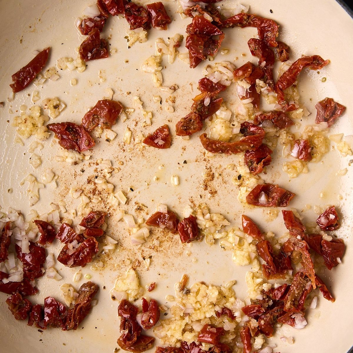 Minced shallot, garlic, and chopped sun-dried tomatoes softening in oil in the bottom of a skillet.