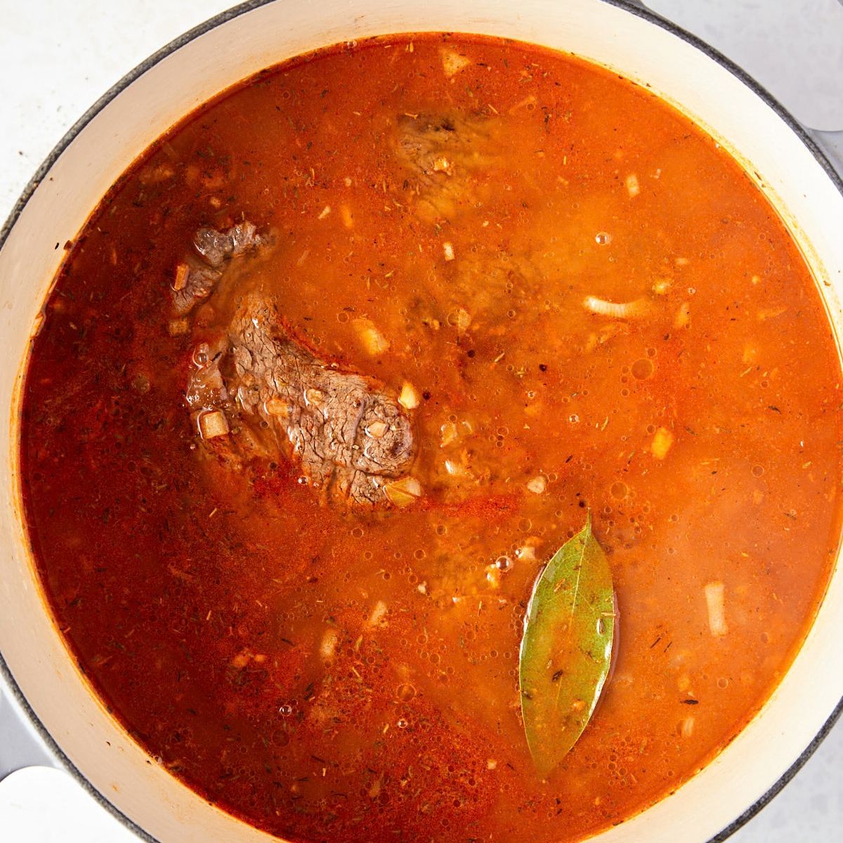 Chuck roast in broth with a bay leaf, ready to braise.