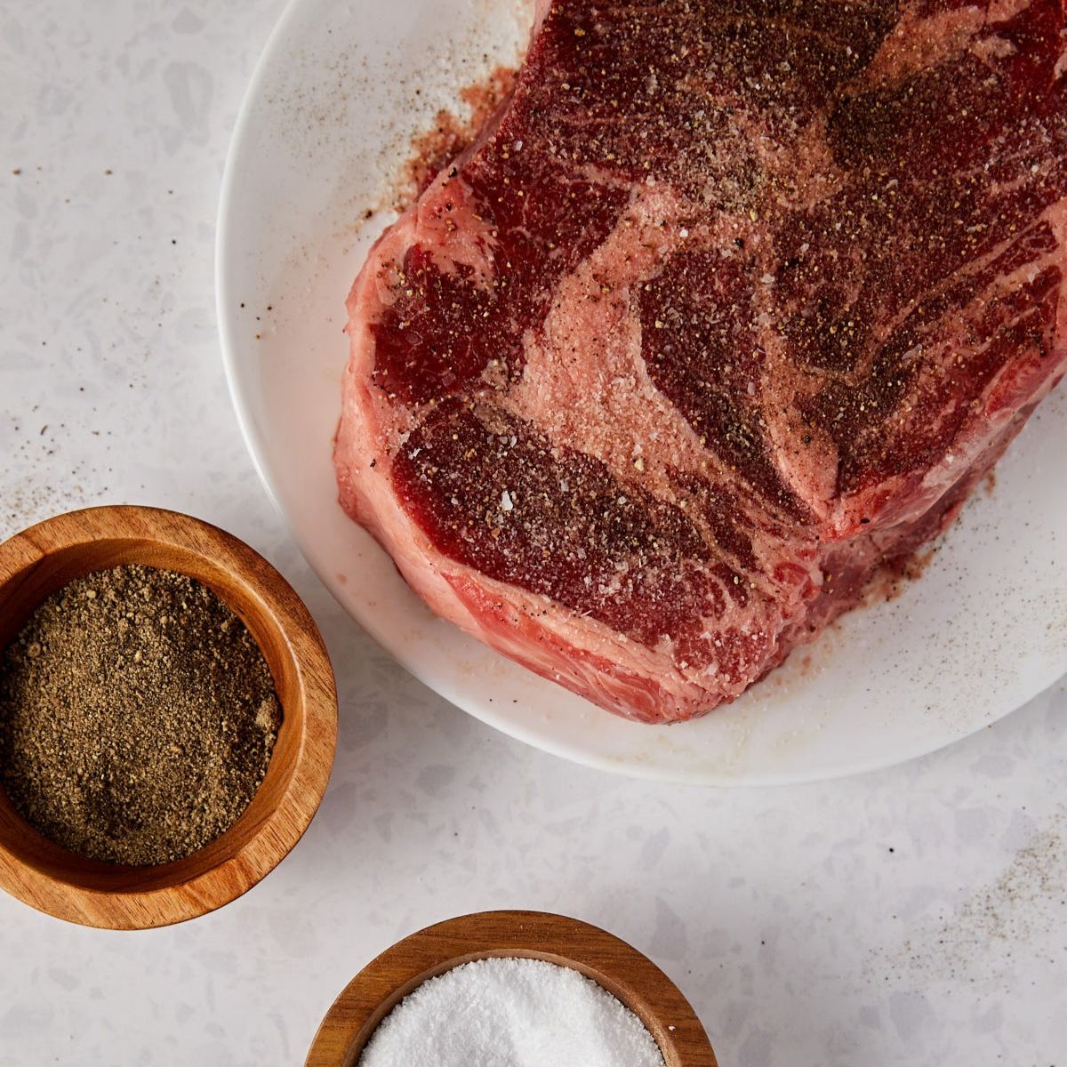Chuck roast seasoned with salt and pepper on a white plate.