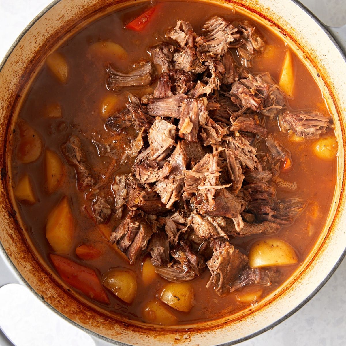 Dutch oven beef stew with shredded beef, potatoes, and carrots.