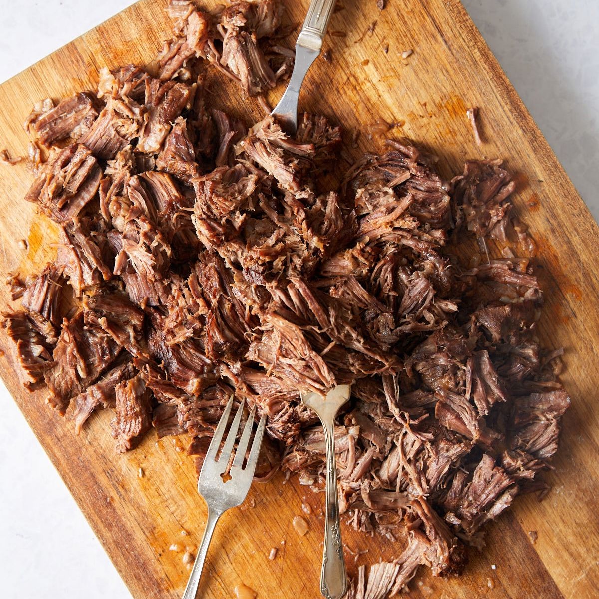 Shredded chuck roast on a wooden cutting board with two forks.