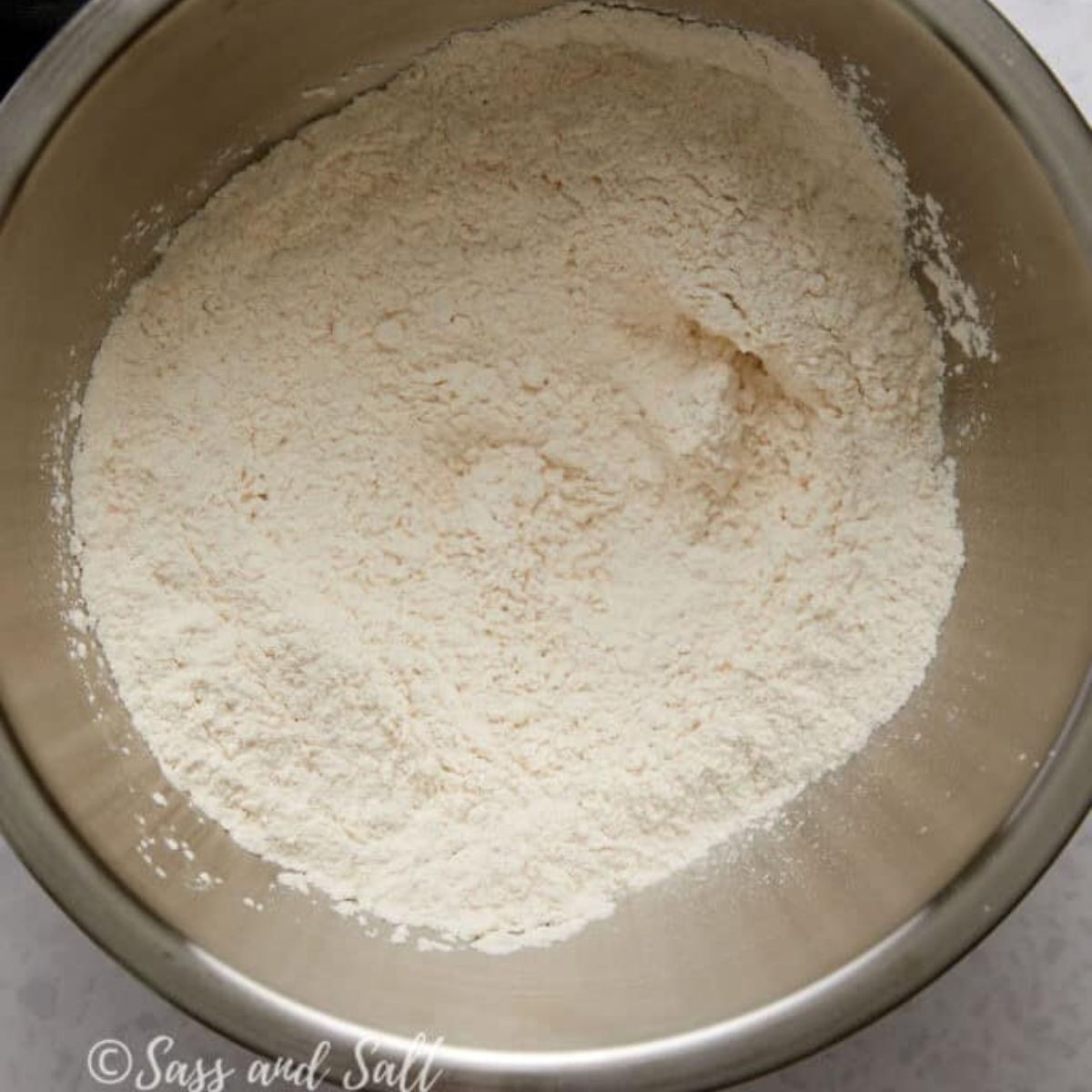Flour, sugar, and salt whisked together in a stainless steel bowl for flaky pie crust.