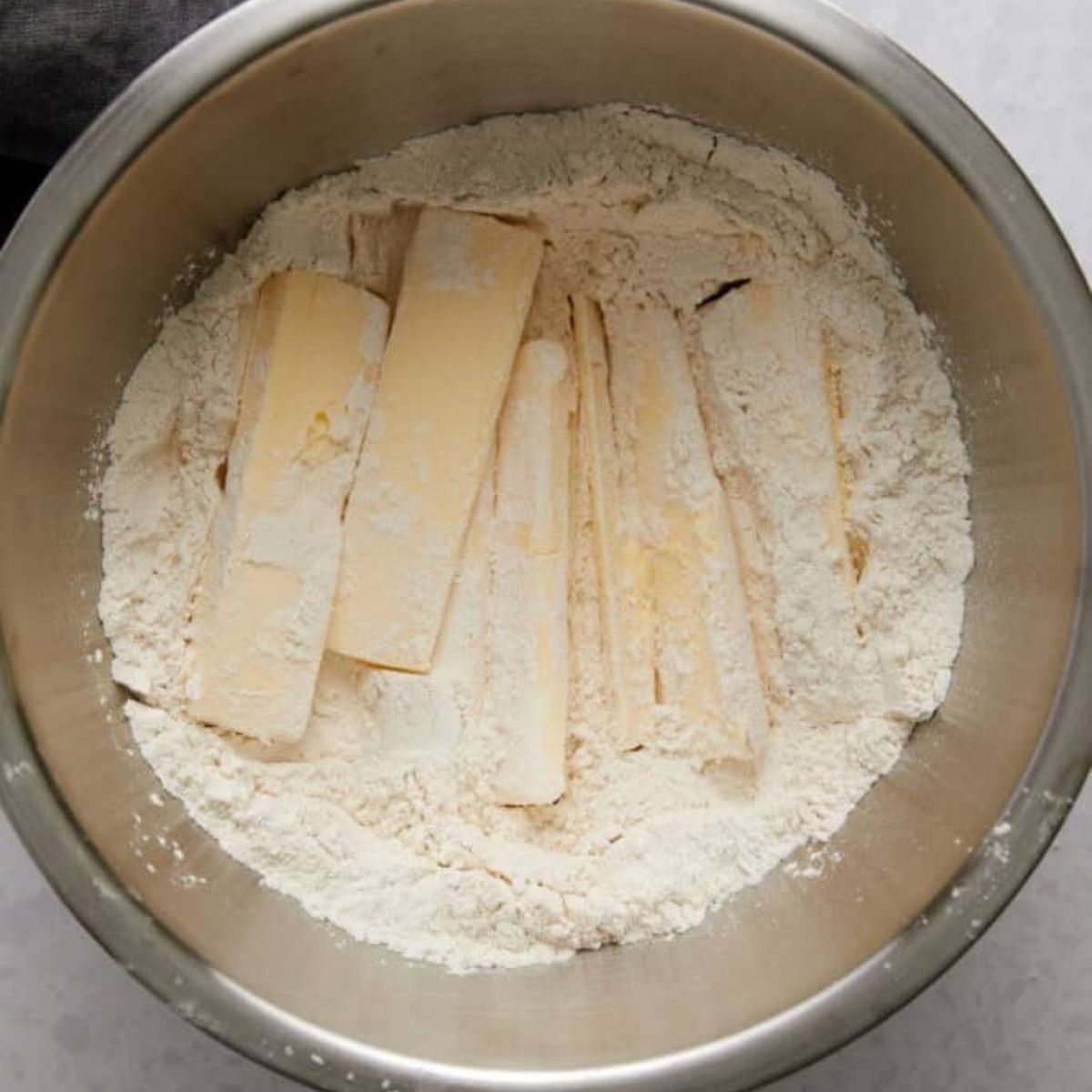 Slices of cold butter tossed in flour in a mixing bowl.