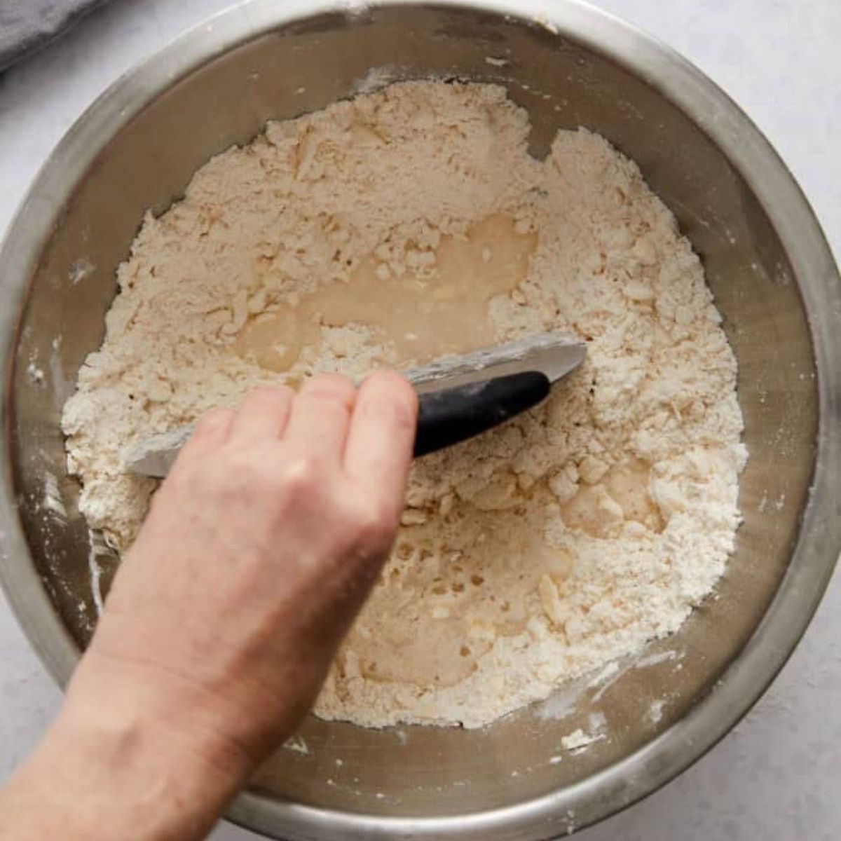 Bench scraper folding ice water into the flour and butter mixture.