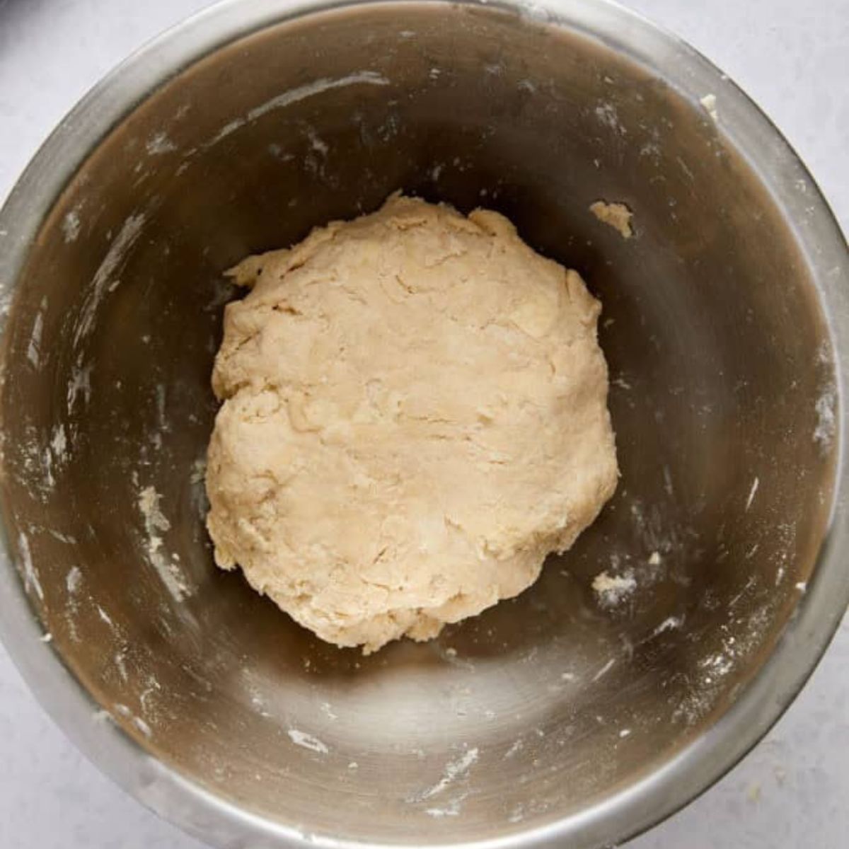 Pie dough pressed into a rough ball in a stainless steel bowl.