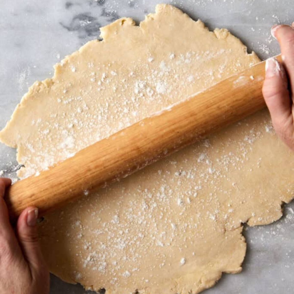 Rolling out pie dough with a wooden rolling pin on a floured marble board.