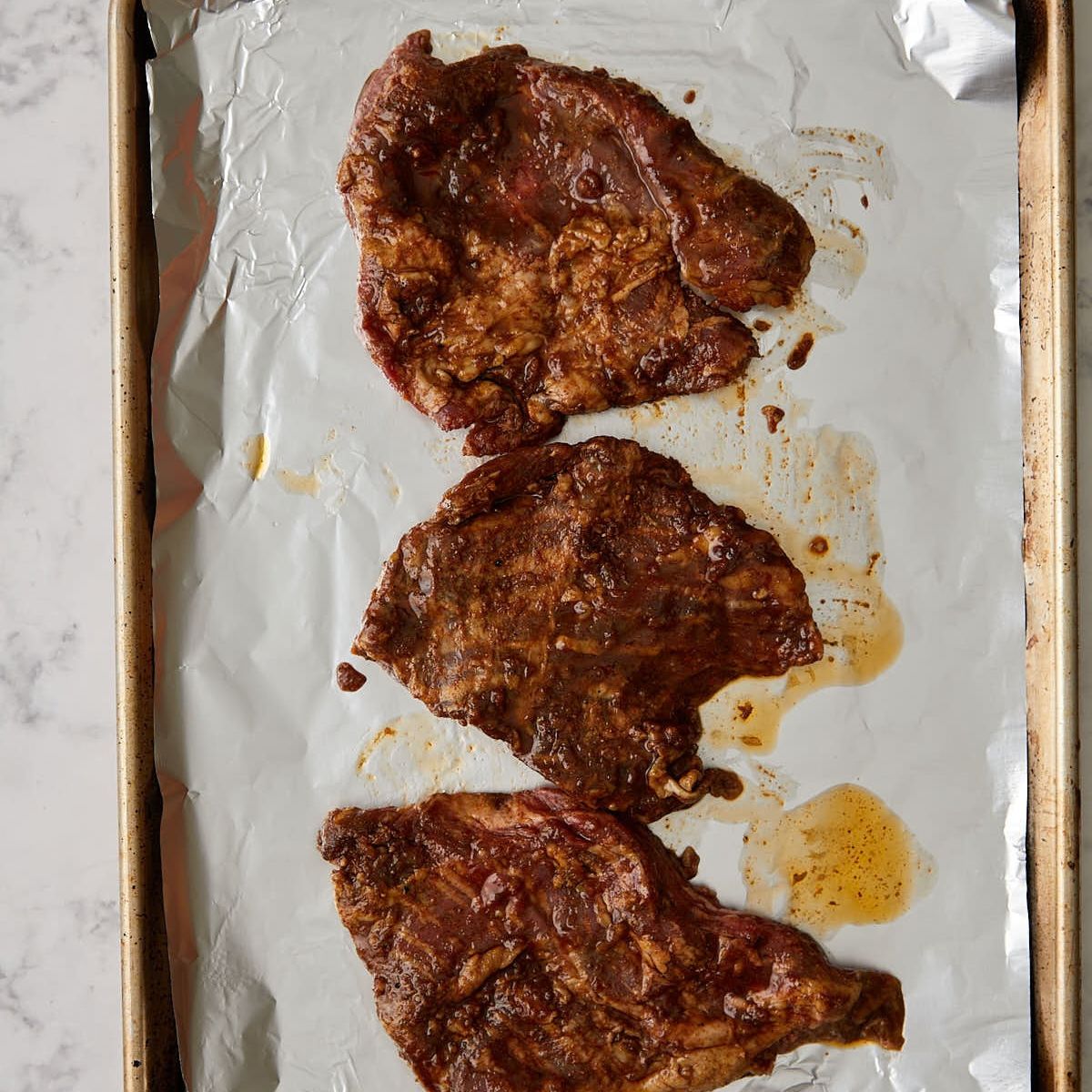 Skirt steak coated in fajita marinade on a foil-lined baking sheet.