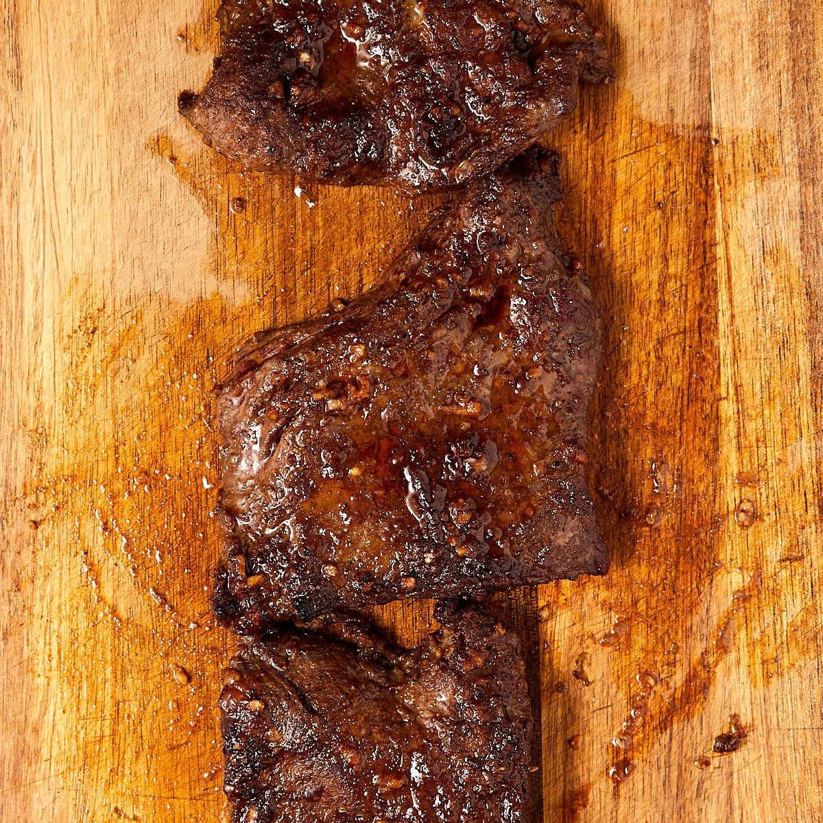 Oven-baked skirt steak pieces, browned and glossy, resting on a wooden cutting board.