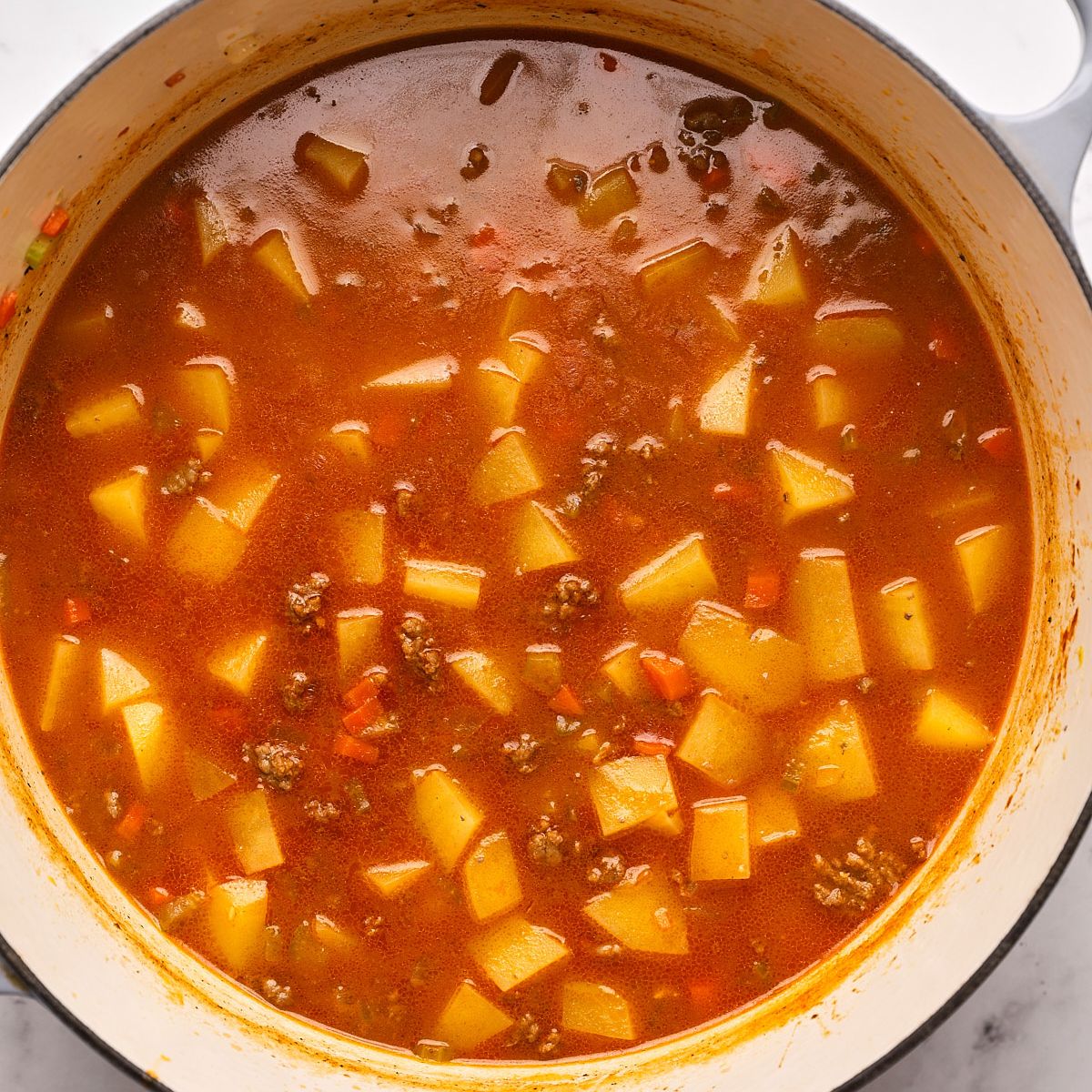 Ground beef, diced potatoes, carrots, and celery simmering in broth in a Dutch oven for cheeseburger soup.