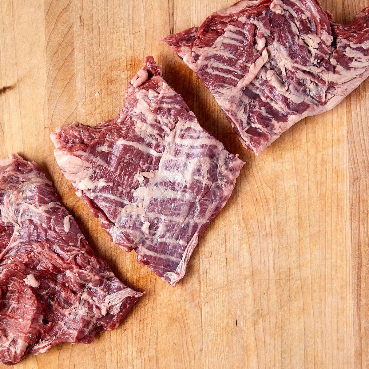 Raw skirt steak cut into 3 pieces on a wooden cutting board, with the grain running across each piece.