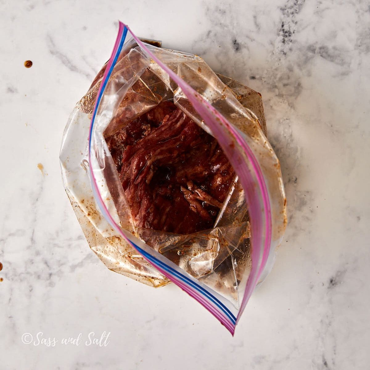 Skirt steak coated in fajita marinade inside a gallon zip-top bag.