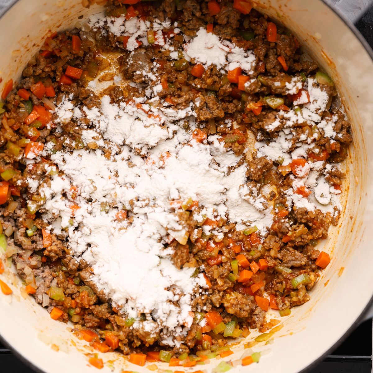 Flour sprinkled over ground beef and diced vegetables in a Dutch oven.
