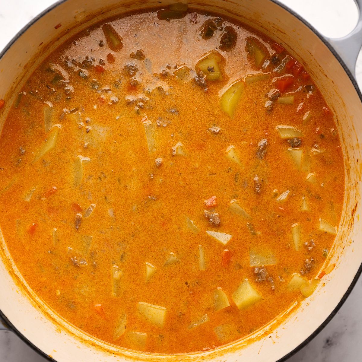 Creamy cheeseburger soup with diced potatoes and ground beef in a Dutch oven after the milk is stirred in.