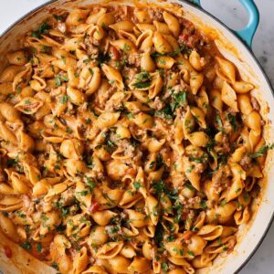 Creamy pasta shells with ground meat and tomato sauce, garnished with fresh herbs in a teal pan.
