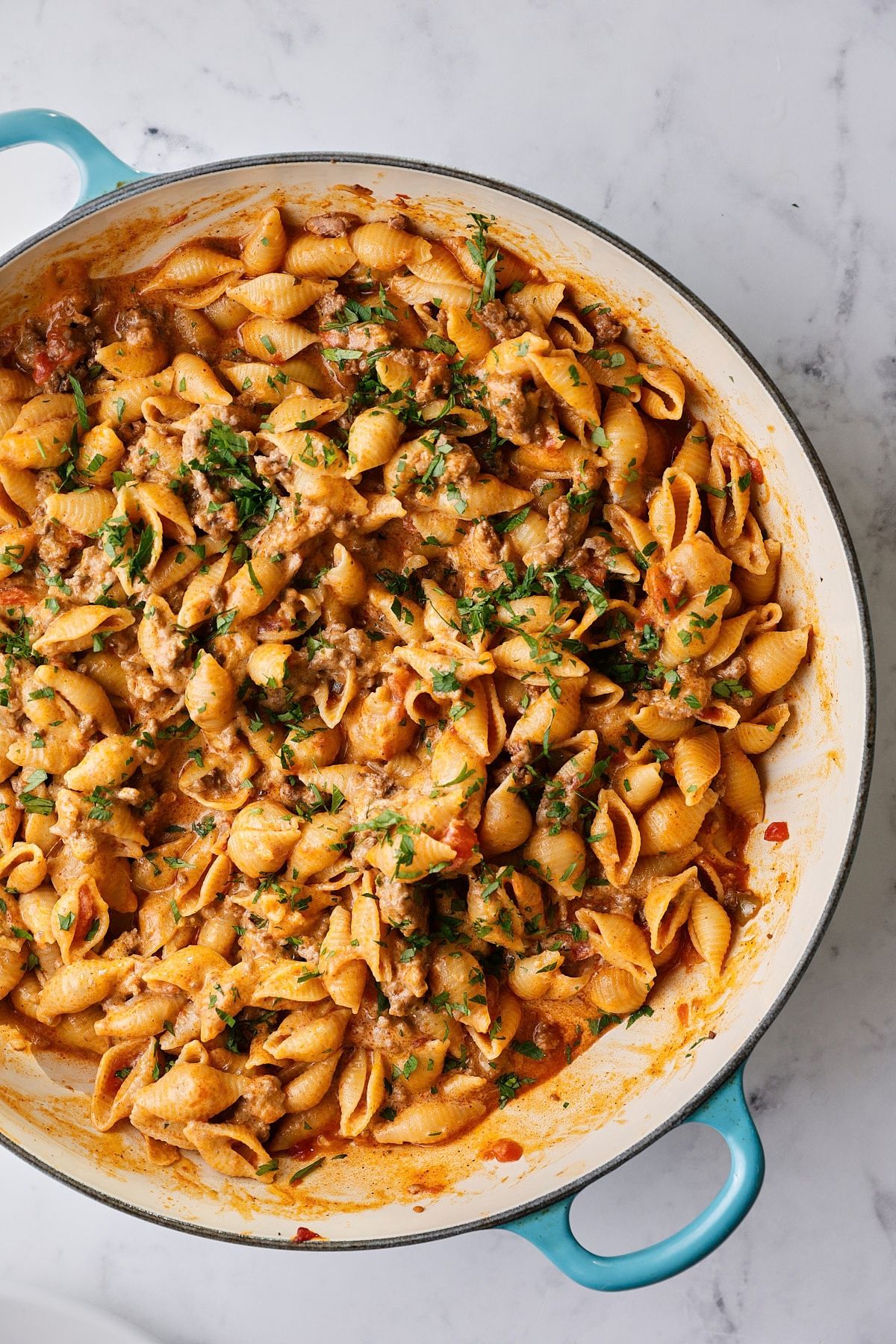 A blue braiser full of creamy taco pasta with ground beef, garnished with chopped parsley.