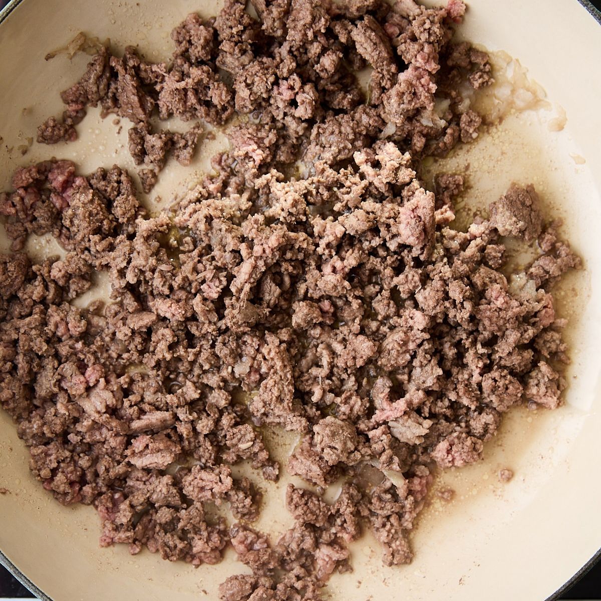 Ground beef and grated onion browning in a blue braiser.